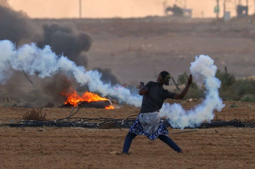 A Palestinian demonstrator throws back a tear gas canister fired by Israeli troops during clashes along the Gaza border