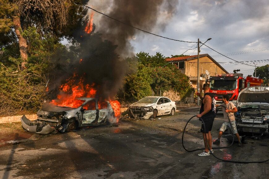 People douse a car blaze in the southern Israeli city of Ashkelon after a rocket attack from Gaza on October 9, 2023.