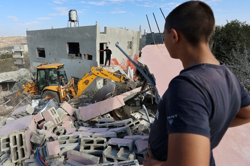 Palestinians look on as an excavator clears the rubble of the West Bank home of exiled Hamas number two Saleh al-Aruri after it was demolished by Israeli forces