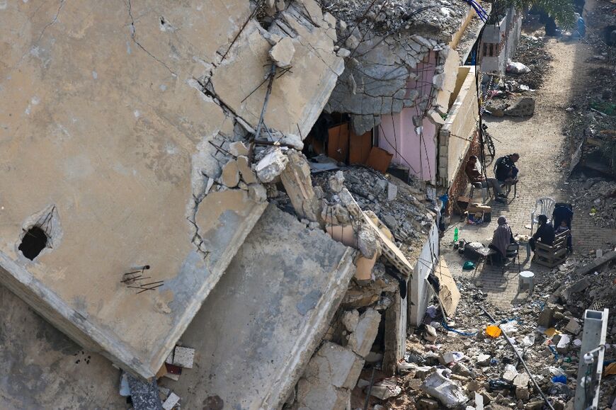 Palestinians sit outside destroyed buildings in the Khezaa district on the outskirts of the southern Gaza city of Khan Yunis