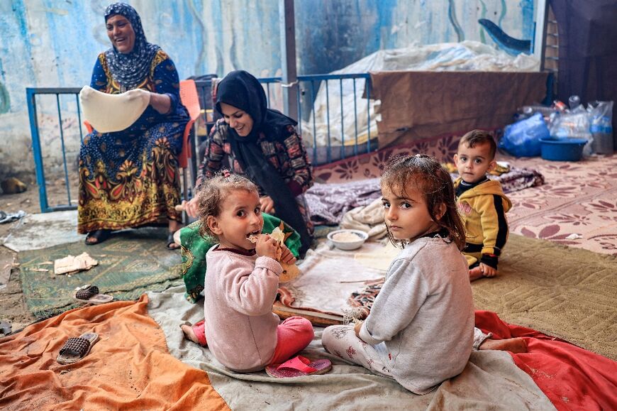 Children sit by a woman preparing bread on an open fire at a school run by the United Nations in Rafah in the southern Gaza Strip on November 14, 2023