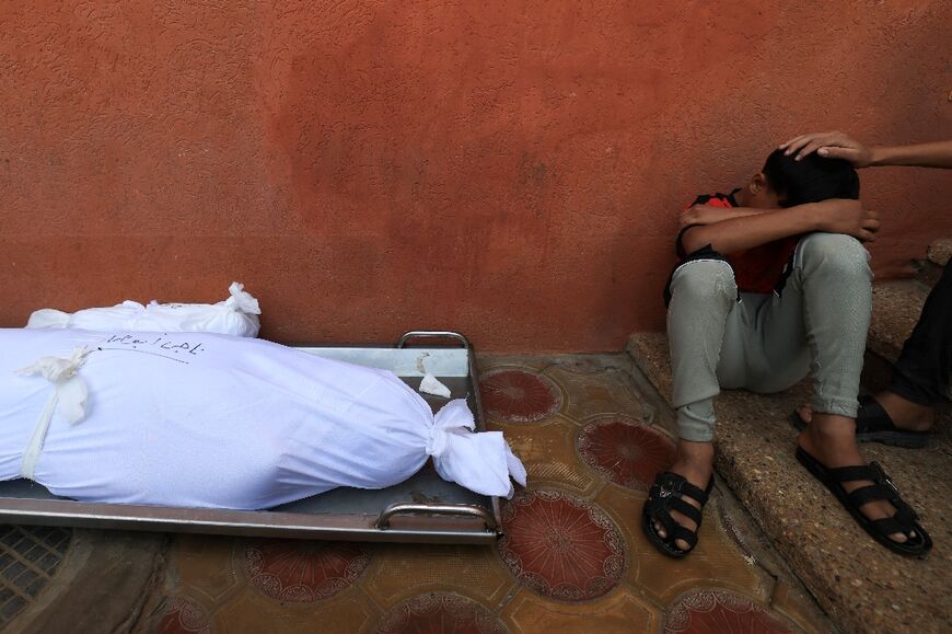 A youth reacts in grief as he sits next to the shrouded bodies of his father and two brothers in Gaza