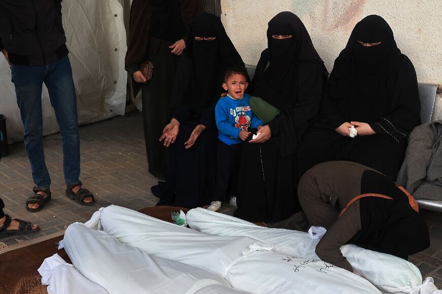 Mourners sit by the shrouded corpses of relatives killed in Israeli bombing on Rafah in the southern Gaza Strip at the morgue of the Al-Najjar hospital on December 3