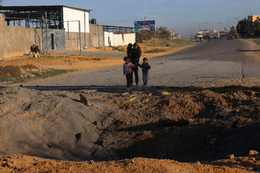 Palestinians fleeing Khan Yunis in the southern Gaza Strip further south toward Rafah stare at a bomb crater in the Salah Al-Din road on December 10, 2023