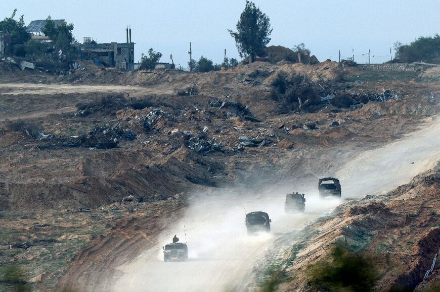 A picture taken from southern Israel on the border with the Gaza Strip on December 27, 2023 shows Israeli army vehicles rolling past the rubble of destroyed buildings in northern Gaza 