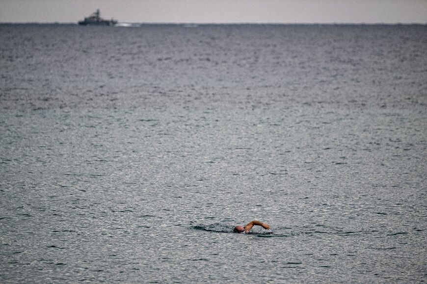 From the seafront, warships are visible beyond the fishermen and swimmers who brave the winter water