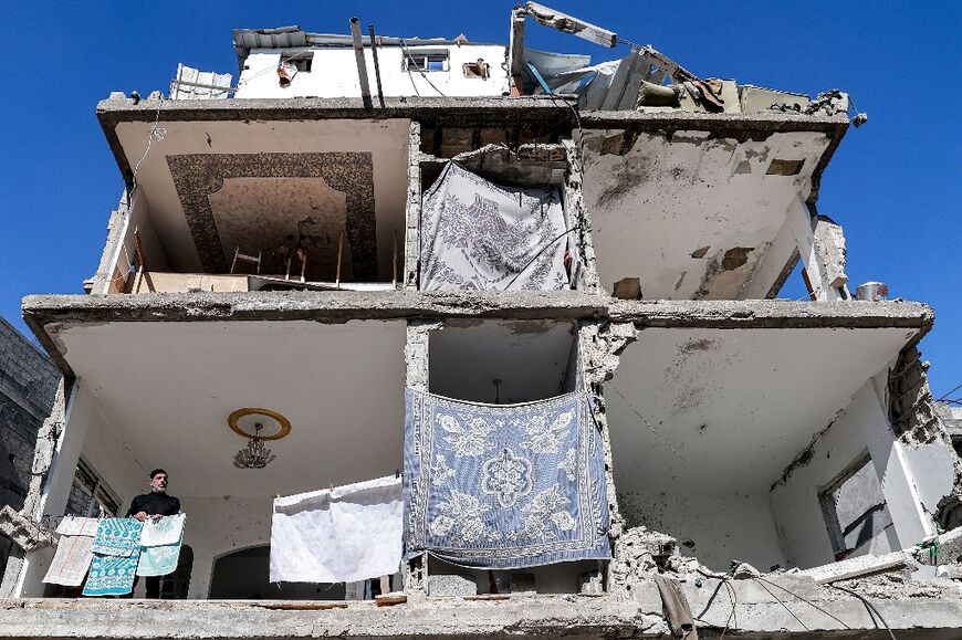 A man stands by towels hanging out to dry in a building with a destroyed facade that was damaged by Israeli bombardment in Rafah