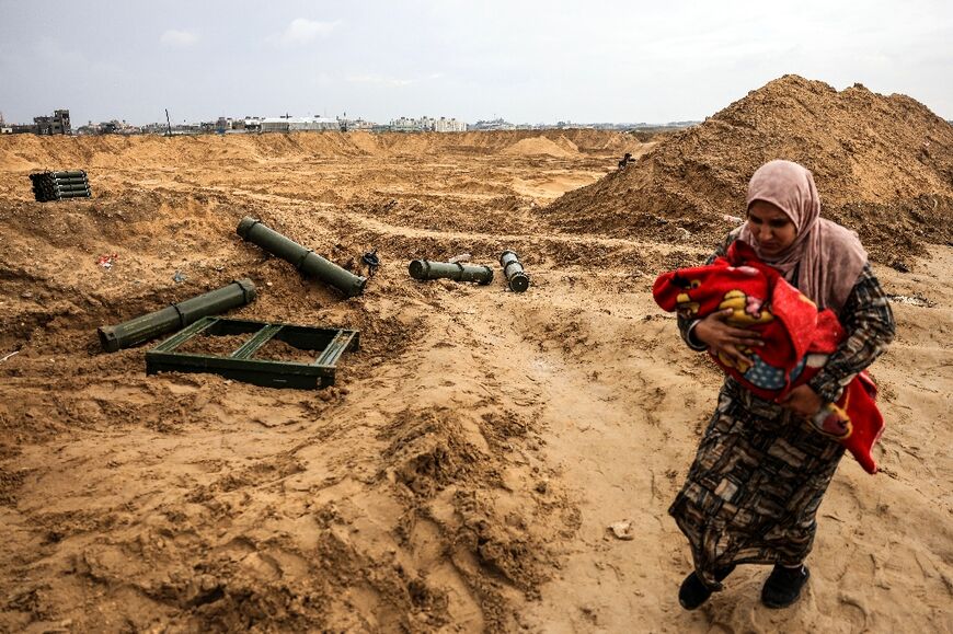 A Palestinian woman holding a baby walks past ammunition containers left behind by Israeli troops as she flees Khan Yunis