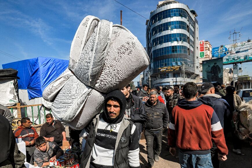 A man walks carrying a folded mattress along a crowded main street in Rafah in the southern Gaza Strip on February 8, 2024