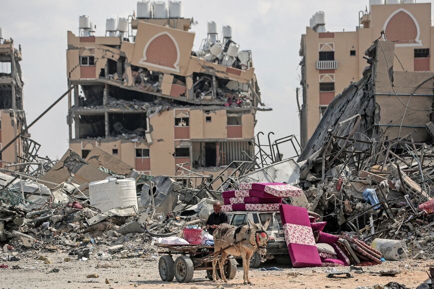 A displaced Palestinian man along with his belongings sits on a donkeycart amid the rubble of houses destroyed by Israeli bombardment in Hamad area, west of Khan Yunis in the southern Gaza Strip