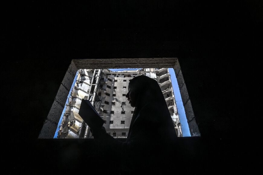 A Palestinian girl reads the Koran near a window that opens onto a building destroyed by the Israeli bombardment of Rafah