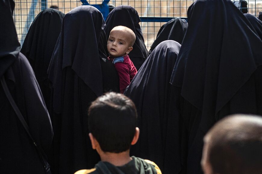 Women stand next to a fence at the al-Hol camp in Syria where Islamic State fighters' families are held