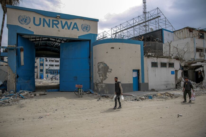 Men carry bags of flour past a damaged compound of the UN agency for Palestinian refugees, after an aid distribution in Gaza City 