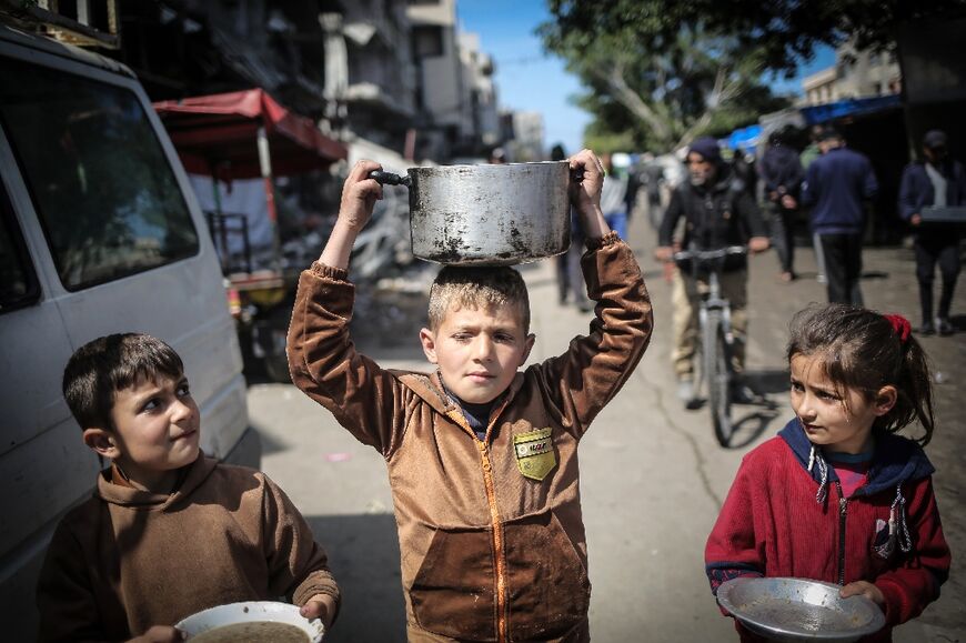 Children clutching pots and pans head for a food distribution point in Khan Yunis