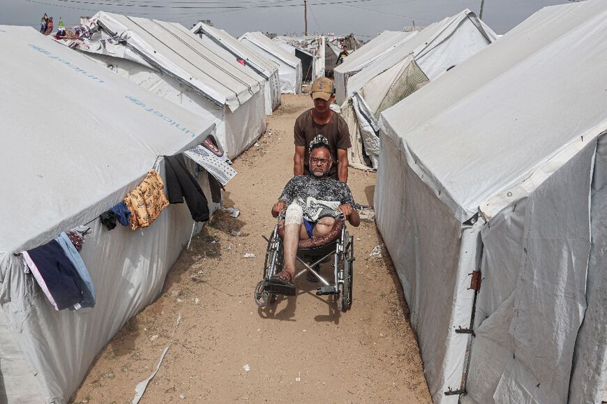 Injured Palestinian Tamer Abu Ali, 47, whose leg was amputated during the Israel-Hamas war, is pushed by his son in a camp for displaced people in Rafah