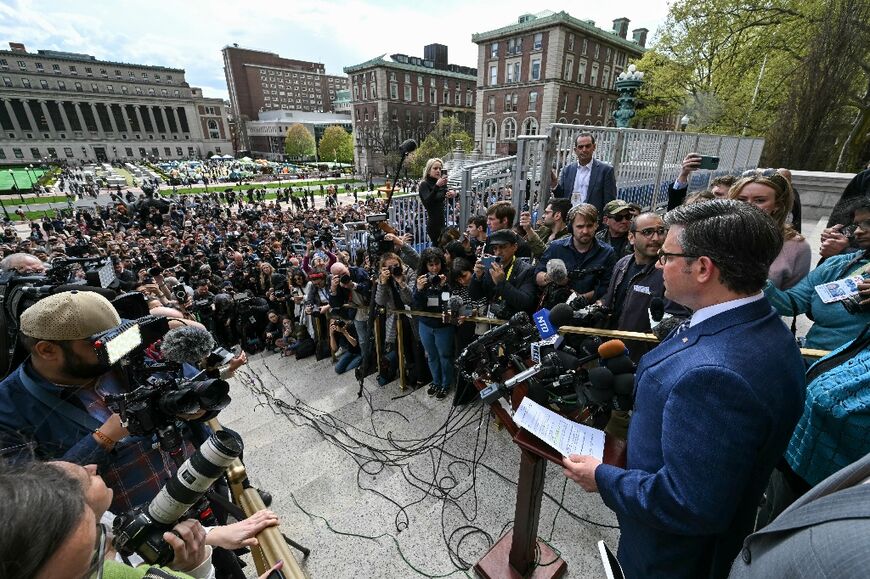 US Speaker of the House Mike Johnson, holding a piece of paper, speaks at Columbia University, with the student pro-Palestinian protest encampment seen in the background