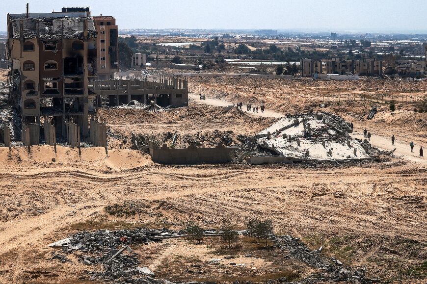 Gazans walk past damaged and destroyed buildings in Khan Yunis Sunday