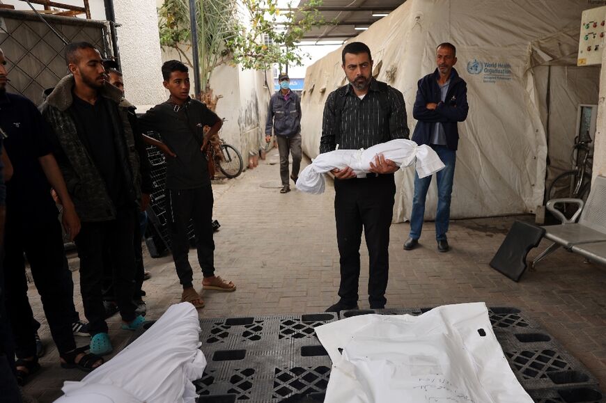 Outside the morgue of a hospital in Rafah, the southern Gaza Strip, a man carries the shrouded body of a child killed in Israeli bombardment