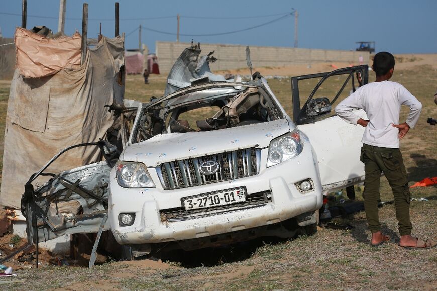 People gather around a car used by US-based aid group World Central Kitchen that was hit by a strike in Deir al-Balah in the central Gaza Strip