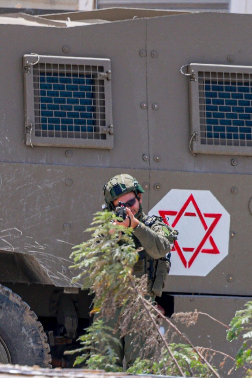 An Israeli soldier takes aim from a position alongside an armoured vehcle during the raid on Jenin