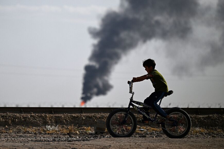 Children play football or ride their bicycles, seemingly unaware of the danger of the gas flaring around them