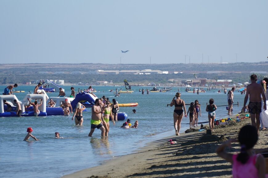 Beachgoers frolic at Lady's Mile in Limassol, Cyprus, as a Eurofighter Typhoon lands at nearby Royal Air Force (RAF) base Akrotiri, on sovereign British territory