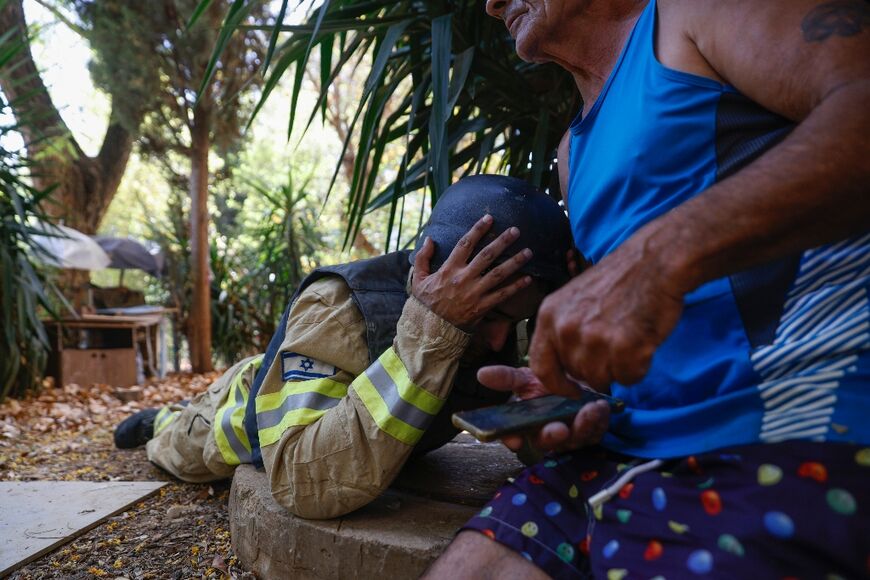 An Israeli firefighter and a resident take cover as sirens sound to warn of rockets launched from southern Lebanon, amid near-daily cross-border clashes