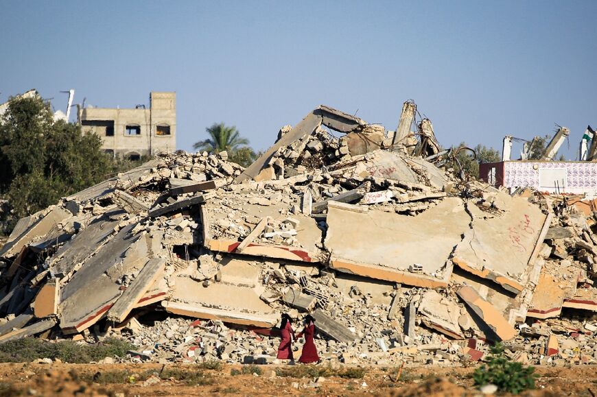 Palestinian women walk past a building that was destroyed during Israeli bombardment of the al-Bureij refugee camp in the central Gaza Strip' on June 24, 2024