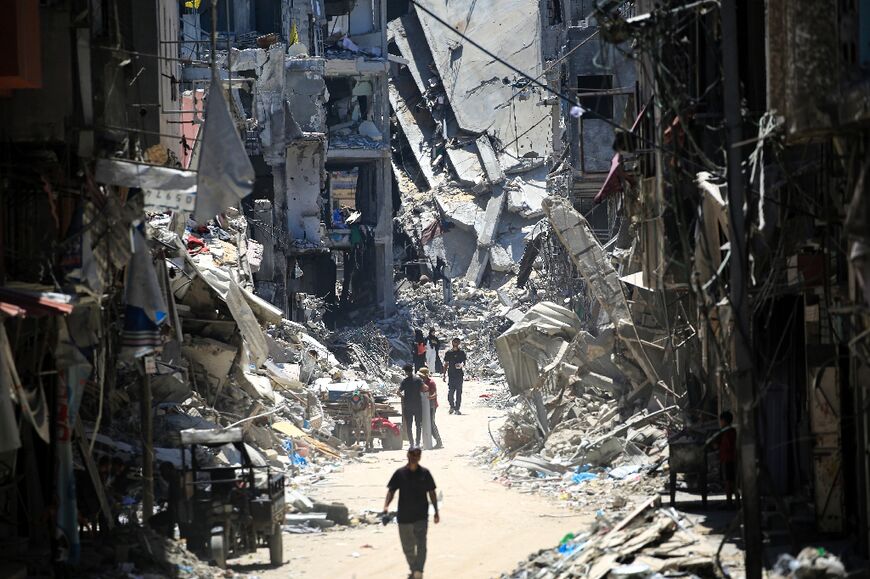 Palestinian men walk along a narrow street past destroyed buildings in Khan Yunis, in the southern Gaza Strip