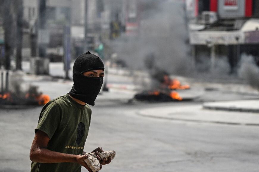 A masked Palestinian youth holds stones during confrontations with Israeli troops in the northern occupied West Bank city of Jenin, on May 22, 2024