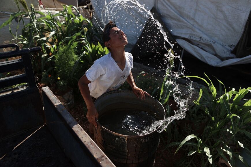 A Syrian youth cools off as he dips his head in a water barrel 