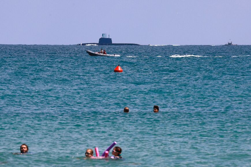 An Israeli navy submarine passes just off Haifa as children swim off the beach