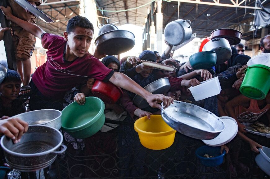 Palestinians hold out dishes to receive vegetable patties prepared by volunteers in northern Gaza's Beit Lahia