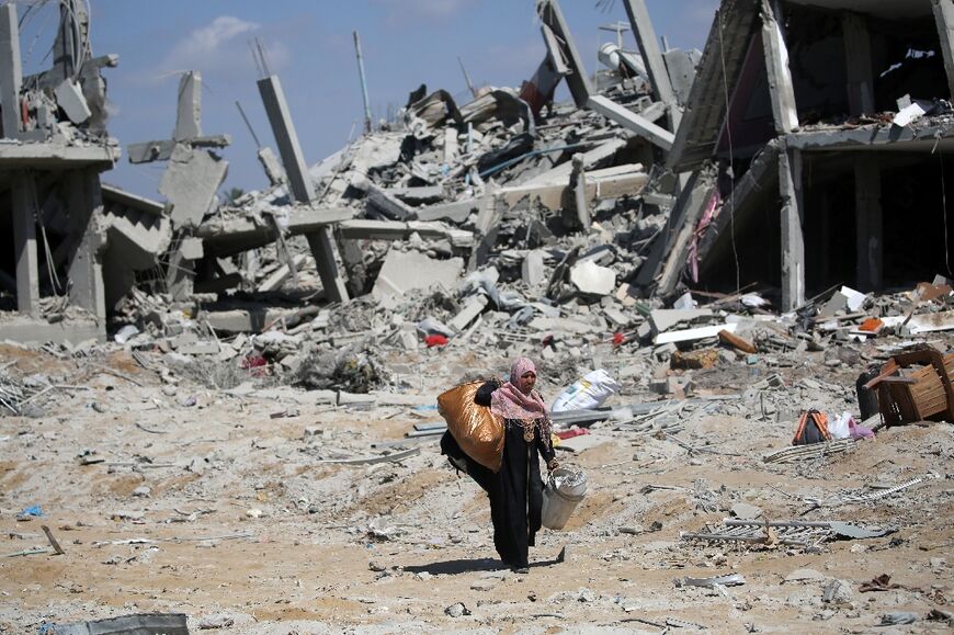 A Palestinian woman walks through a bombed out neighbourhood of Deir el-Balah carrying what belongings she was able to salvage from the rubble of her home