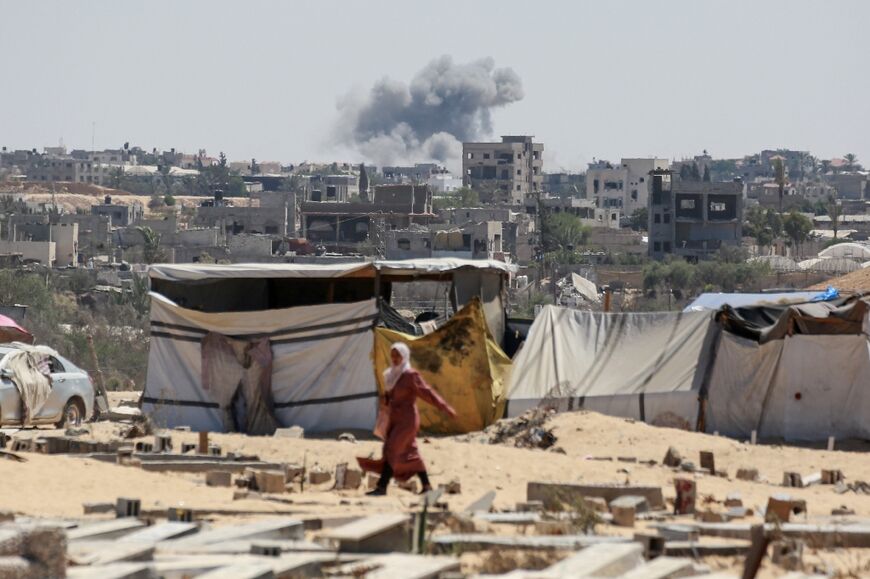 A woman walks in Khan Yunis in the southern Gaza Strip as smoke billows after an Israeli bombardment