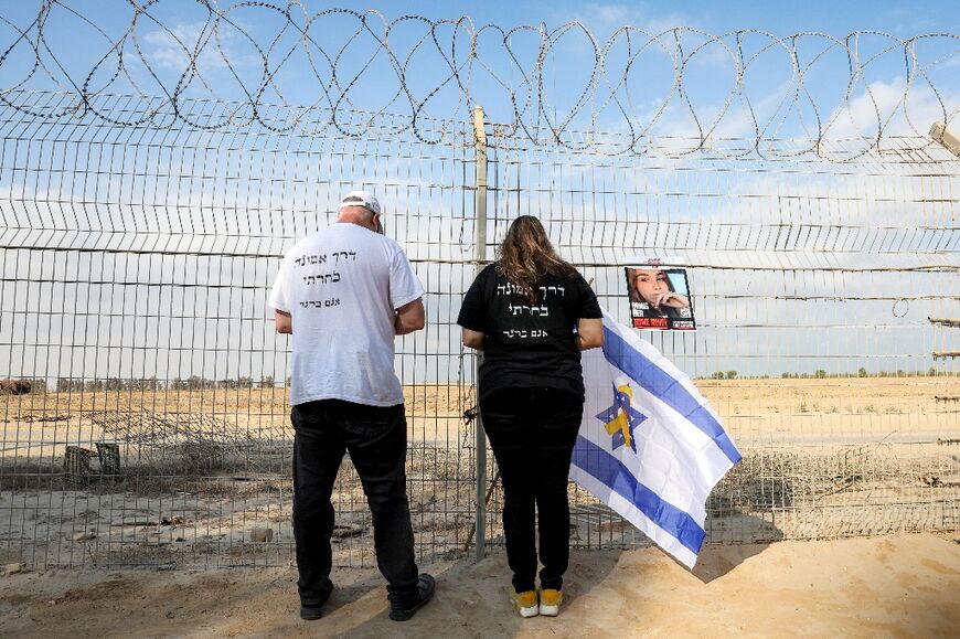 A man and woman stand near a poster identifying Israeli hostage Agam Berger hanging on a barbed-wire fence