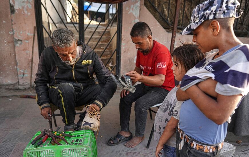 Palestinians wait for a cobbler to repair their shoes in Khan Yunis in the southern Gaza Strip