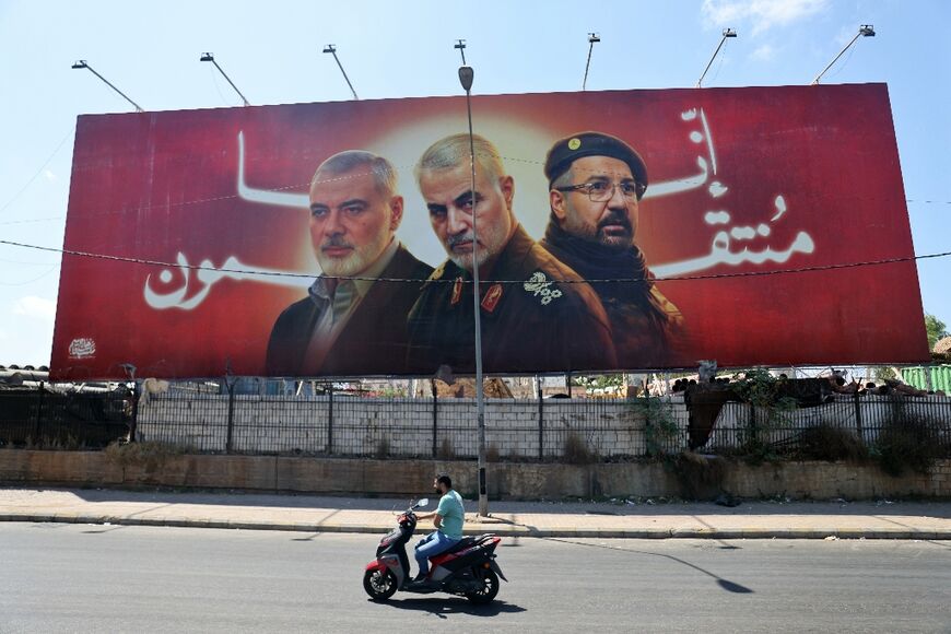 A man rides his moped past a billboard in Beirut bearing portraits of slain Hezbollah and Iranian figures Ismail Haniyeh, Qasem Soleimani and Fuad Shukr bearing the message 'we will seek revenge'