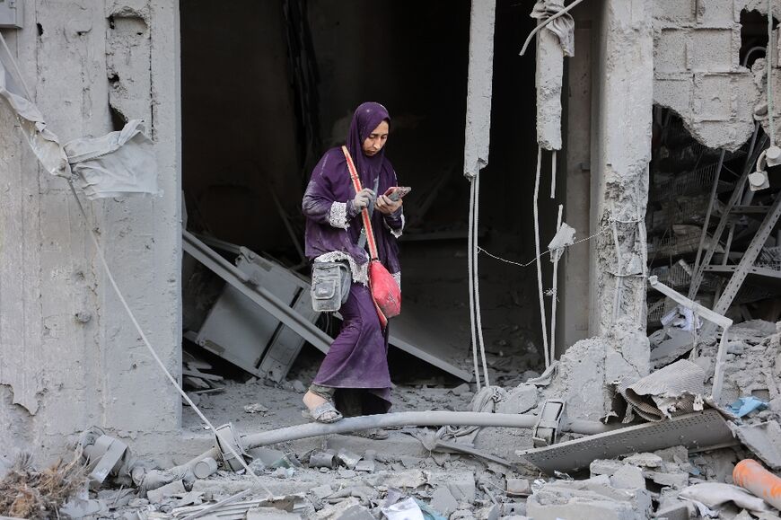 A woman checks her phone amid the rubble of a building destroyed by Israeli bombardment in Gaza City's Sheikh Radwan district