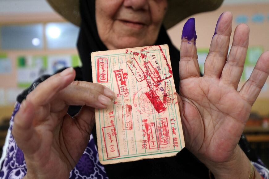 A voter displays her ink-stained finger and card after casting her ballot in Algiers