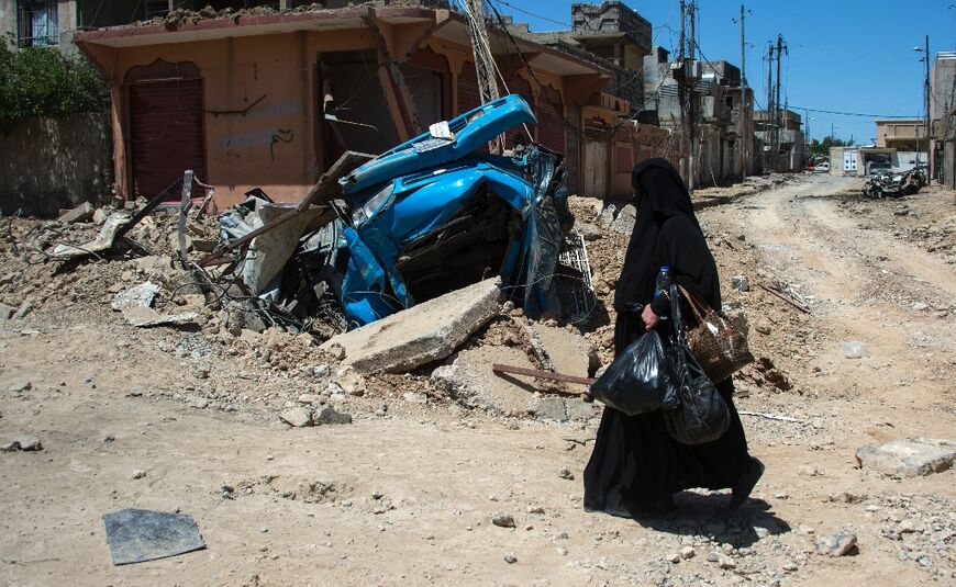 A displaced Iraqi walks past a destroyed vehicle in a neighbourhood of west Mosul on May 17, 2017, during an Iraqi forces offensive to retake the area from Islamic State group fighters