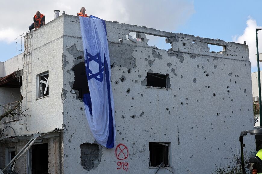 People hang a giant Israeli flag from the roof of a damaged building in Kiryat Bialik in the Haifa district of northern Israel, which Lebanon's Hezbollah said it had targeted