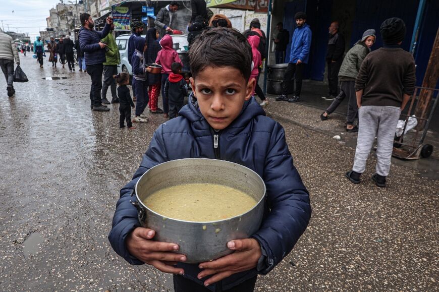 A displaced Palestinian child carries a ration of red lentil soup, distributed by volunteers in Rafah in the southern Gaza Strip