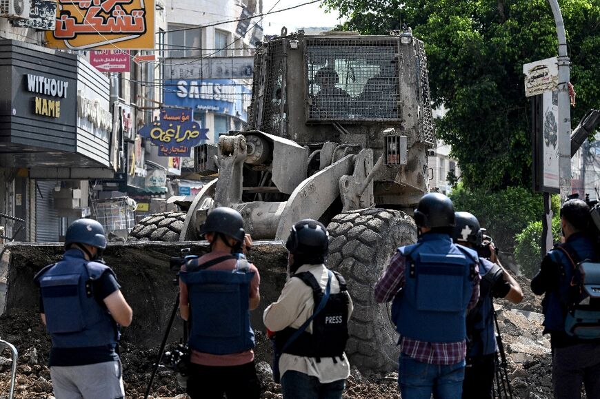 An Israeli bulldozer tears up a street in the occupied West Bank city of Jenin as journalists film