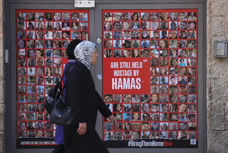 Palestinians pass a store entrance in Jerusalem displaying portraits of Israelis held hostage by Palestinian militants in Gaza 