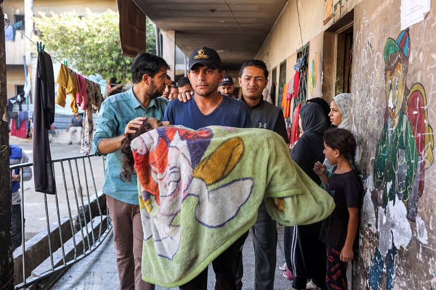 At Rafei school in Jabalia refugee camp, a man carries the blanket-wrapped body of a girl who killed in bombardment 