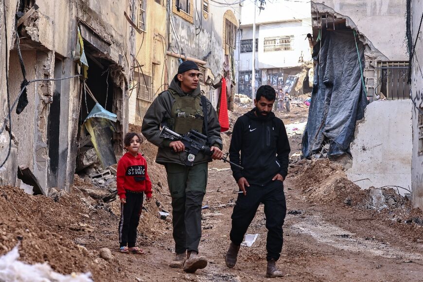 A Palestinian gunman and a resident walk amid destruction in Jenin following the Israeli raid