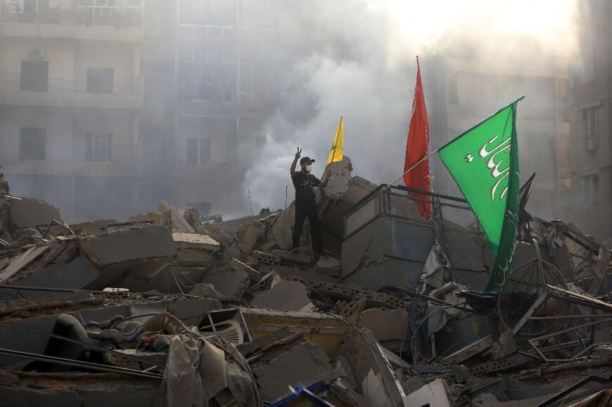 A man poses with Hezbollah banners on the rubble of a building flattened by a pre-dawn Israeli air strike on the Mreijeh district of Beirut’s southern suburbs