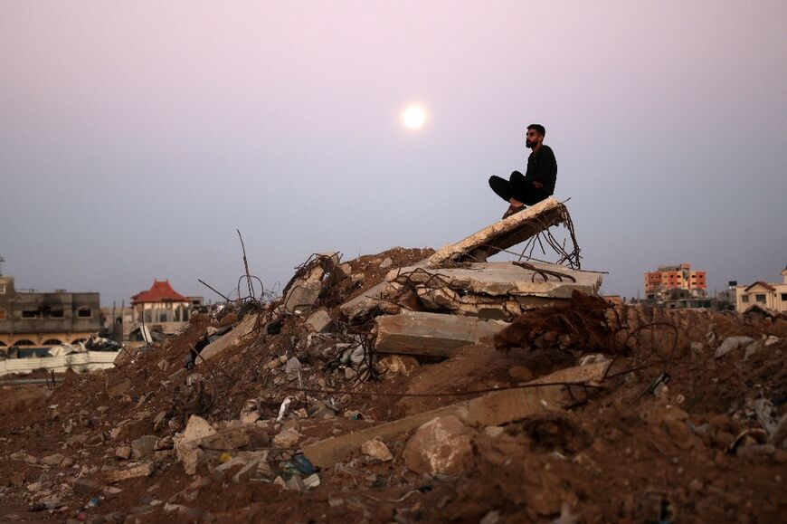 The full moon rises behind a man sitting atop a pile of rubble at al-Bureij refugee camp in central Gaza 