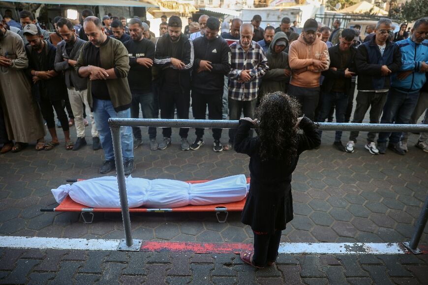 A girl watches as mourners pray over the body of a victim of an Israeli strike during a funeral at al-Aqsa Martyrs Hospital in Deir Al-Balah in the central Gaza Strip 